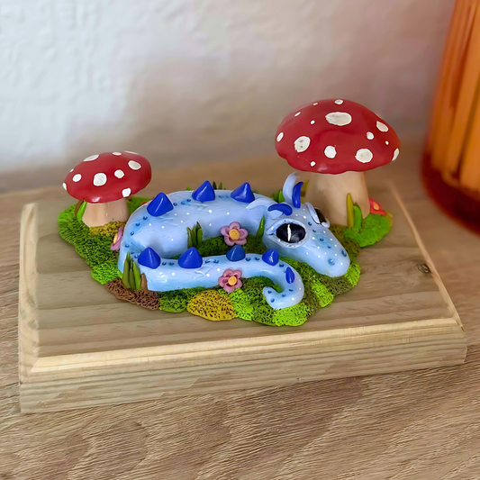 Whimsical Blue Dragon Figure Laying Amongst The Mushrooms.