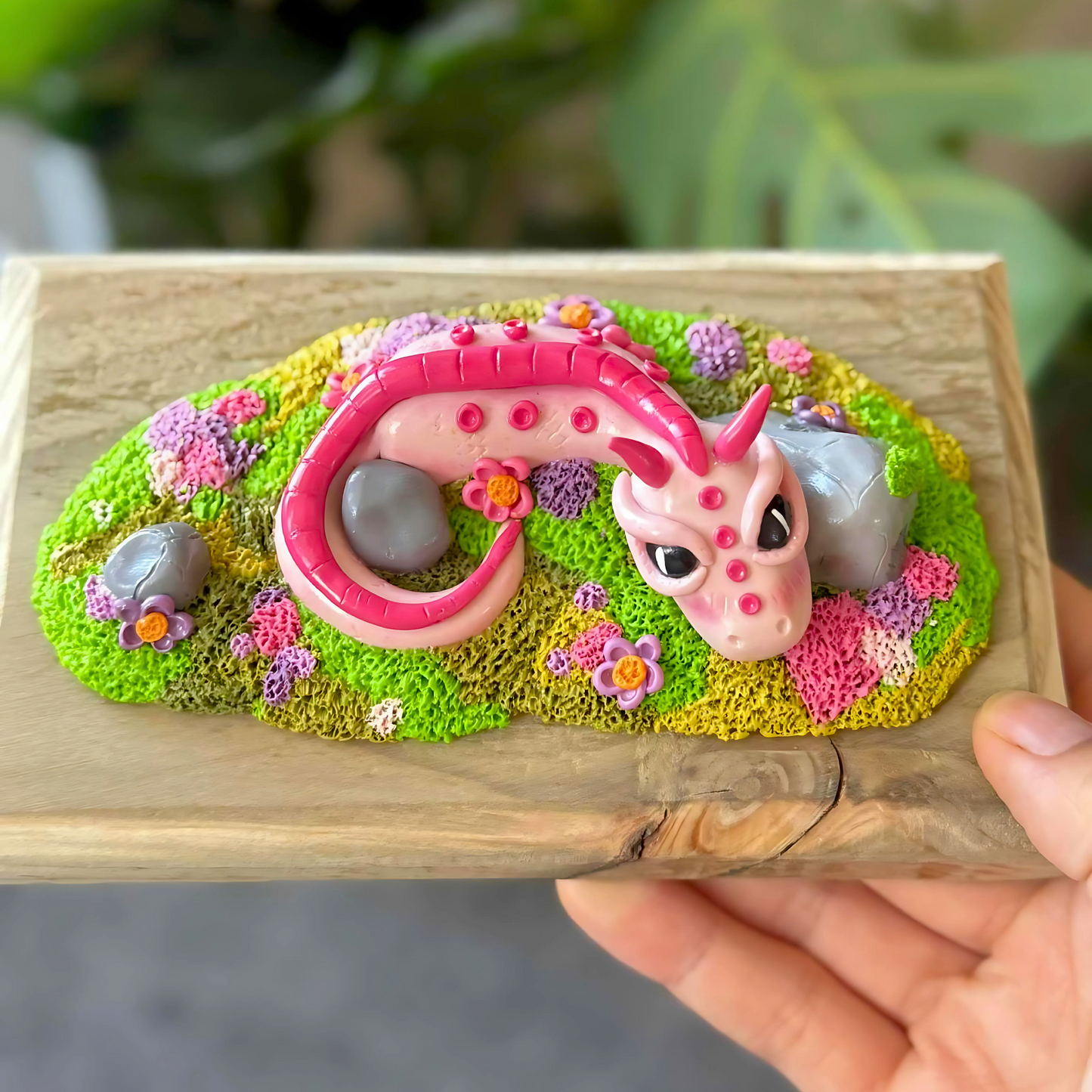 Whimsical Pink Dragon Figure Laying Amongst The Rocks.